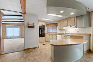 Kitchen with a peninsula, cream cabinetry, light countertops, and white dishwasher
