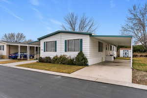 Manufactured / mobile home with an attached carport, concrete driveway, a front lawn, and covered porch