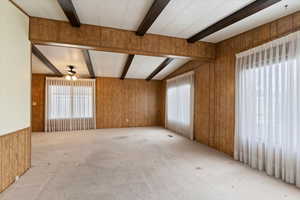 Spare room featuring wooden walls, carpet floors, beam ceiling, and a ceiling fan
