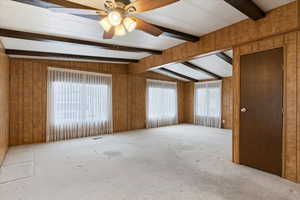 Spare room featuring a ceiling fan, carpet, wooden walls, plenty of natural light, and lofted ceiling with beams