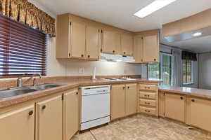 Kitchen featuring light countertops, white dishwasher, cream cabinetry, stone finish flooring, and a peninsula
