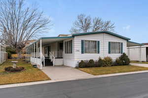 Manufactured / mobile home featuring a porch, a carport, a front yard, and concrete driveway