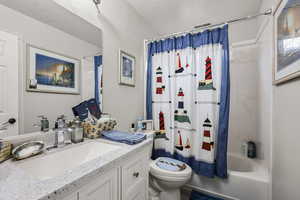 Full bathroom with a textured wall, a textured ceiling, shower / bathtub combination with curtain, and vanity