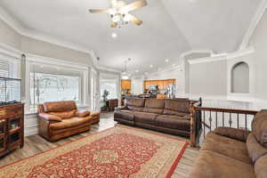 Living area with ceiling fan, ornamental molding, light wood finished floors, vaulted ceiling, and a decorative wall