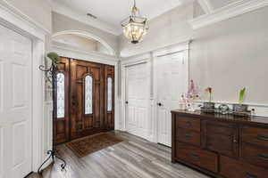 Foyer entrance with light wood-style flooring, suspended lighting, and crown molding