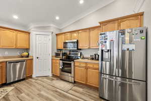 Kitchen featuring stainless steel appliances, ornamental molding, lofted ceiling, light countertops, and light wood finished floors