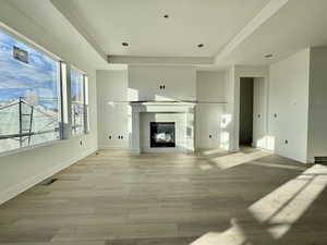 Unfurnished living room with light wood finished floors, a glass covered fireplace, a tray ceiling, and recessed lighting