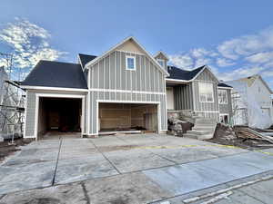 View of front of house with board and batten siding, concrete driveway, and roof with shingles