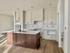 Two tone kitchen featuring light wood finished floors, light stone countertops, an island with sink, backsplash, and dual tone cabinets