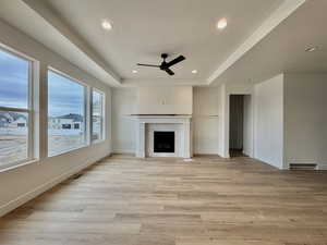 Unfurnished living room with a ceiling fan, a tray ceiling, light wood-style flooring, a fireplace, and recessed lighting