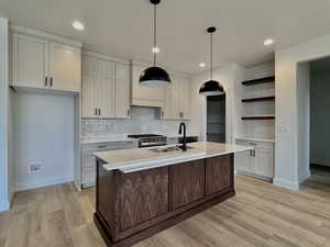 Kitchen with tasteful backsplash, light wood-style floors, light stone counters, hanging light fixtures, and gas range