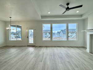 Unfurnished living room featuring a chandelier, healthy amount of natural light, a ceiling fan, light wood-style flooring, and a raised ceiling