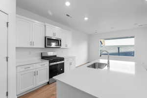 Kitchen featuring stainless steel appliances, light wood finished floors, white cabinetry, recessed lighting, and light stone countertops