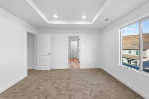 Unfurnished bedroom featuring light carpet and a raised ceiling