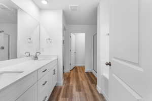 Full bath featuring a shower stall, double vanity, and dark wood-type flooring