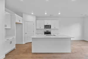 Kitchen featuring white cabinetry, light wood-type flooring, an island with sink, stainless steel appliances, and light stone countertops