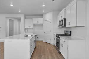 Kitchen featuring stainless steel appliances, white cabinets, a center island with sink, recessed lighting, and light stone countertops
