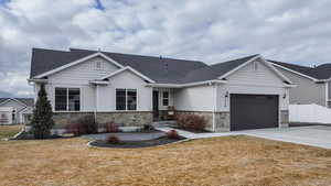 View of front of property with stone siding, driveway, a shingled roof, and an attached garage