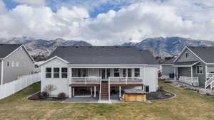 Back of house with a hot tub, a patio area, a deck with mountain view, and a shingled roof