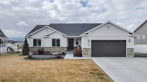 View of front of home featuring stone siding, a front yard, driveway, and a garage