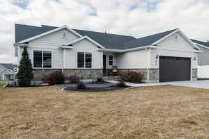 View of front facade featuring a front yard, stone siding, a shingled roof, and a garage