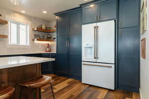 Kitchen featuring white refrigerator with ice dispenser, a kitchen bar, dark wood-style flooring, open shelves, and recessed lighting