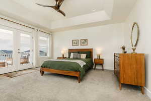 Bedroom featuring french doors, light carpet, access to outside, a tray ceiling, and ceiling fan