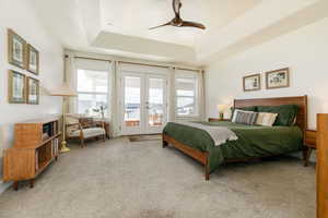 Carpeted bedroom with french doors, access to exterior, multiple windows, ceiling fan, and a tray ceiling
