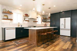 Kitchen with open shelves, white appliances, a kitchen bar, pendant lighting, and dark wood-style flooring