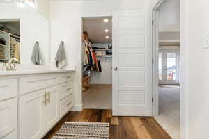 Bathroom featuring a walk in closet, vanity, dark wood-style floors, dark colored carpet, and recessed lighting