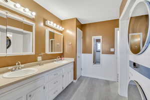 Full bathroom with wainscoting, double vanity, stacked washer and dryer, and light wood-style flooring