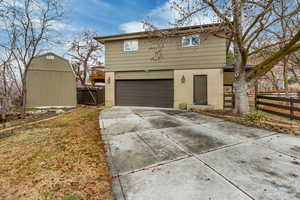 View of side of property with an attached garage, concrete driveway, brick siding, a gate, and a storage shed