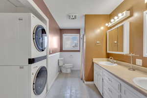 Bathroom with a shower with curtain, double vanity, stacked washer and dryer, and a wainscoted wall