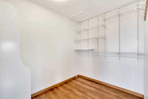 Walk in closet with light wood finished floors and attic access