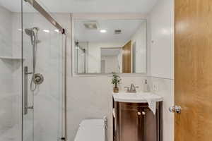 Bathroom featuring vanity, a marble finish shower, and tile walls