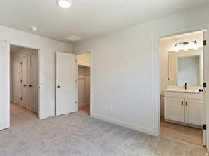 Unfurnished bedroom featuring light colored carpet, ensuite bath, a spacious closet, and a textured ceiling