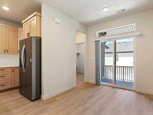 Kitchen featuring stainless steel fridge with ice dispenser, light countertops, light wood finish cabinets, light wood-type flooring, and tasteful backsplash