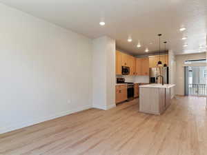 Kitchen featuring light wood finish cabinetry, stainless steel appliances, a center island with sink, pendant lighting, and light wood-style floors