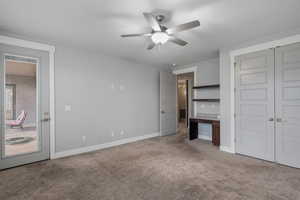 Unfurnished bedroom featuring light carpet, ceiling fan, an office area, and a closet