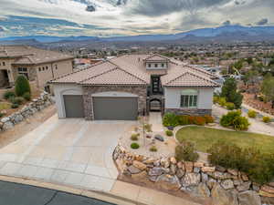 Mediterranean / spanish-style home featuring stone siding, stucco siding, a garage, a mountain view, and driveway