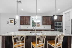 Kitchen featuring dark wood finish cabinets, a kitchen breakfast bar, tasteful backsplash, a center island with sink, and light stone counters