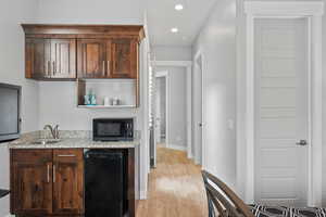 Kitchen featuring black appliances, open shelves, light stone counters, dark wood finish cabinets, and light wood-style floors