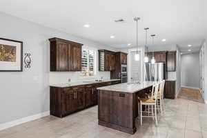 Kitchen featuring tasteful backsplash, a kitchen bar, dark wood finish cabinetry, decorative light fixtures, and a center island with sink