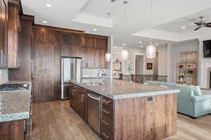 Kitchen with a raised ceiling, ornamental molding, open floor plan, light wood-type flooring, and an island with sink
