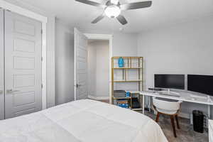Bedroom with dark colored carpet, ceiling fan, and an office area