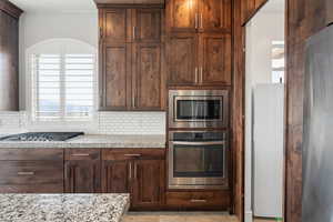 Kitchen featuring stainless steel appliances, backsplash, light stone counters, and dark wood finish cabinetry