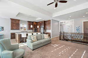 Living room with crown molding, a ceiling fan, a raised ceiling, light colored carpet, and recessed lighting