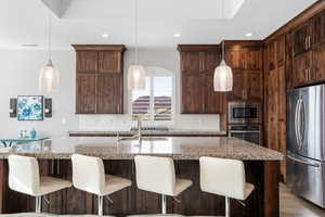 Kitchen featuring stainless steel appliances, dark wood finish cabinetry, an island with sink, a kitchen breakfast bar, and crown molding