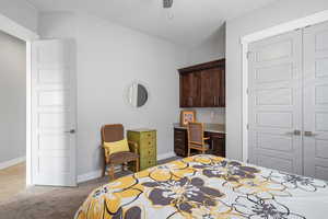 Bedroom featuring light carpet, a closet, built in desk, and ceiling fan
