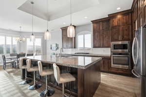 Kitchen with stainless steel appliances, light stone counters, a kitchen bar, decorative backsplash, and light wood finished floors